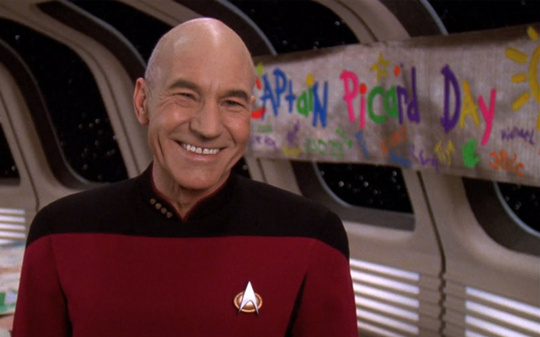 Capt Picard smiling in front of a banner saying Capt Picard Day